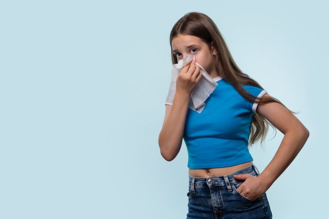 Girl wiping nose with tissue, showing signs of cold