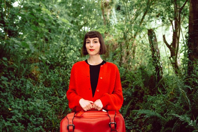 Woman in red with big red suitcase in forest