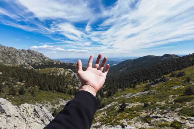 Person stretching hand to blue sky above mountain valley