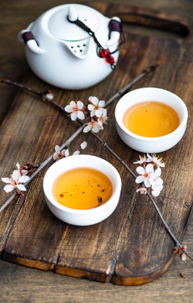Cups of green tea with floral petals on wooden board with tea pot