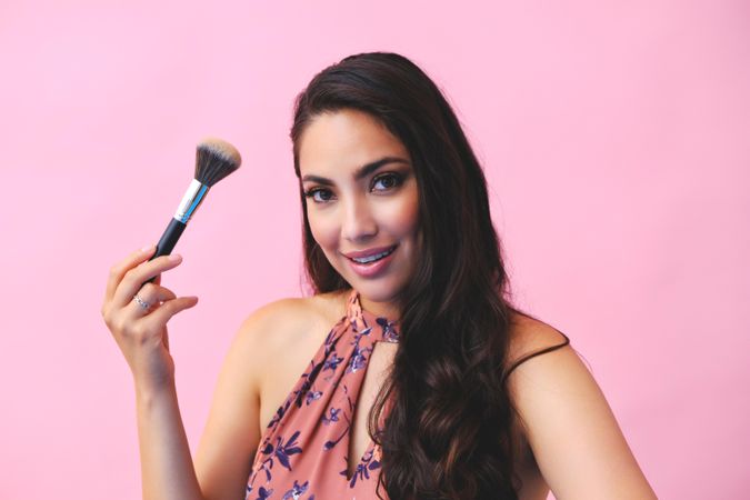 Head shot of Hispanic woman looking at camera while holding up large make up brush