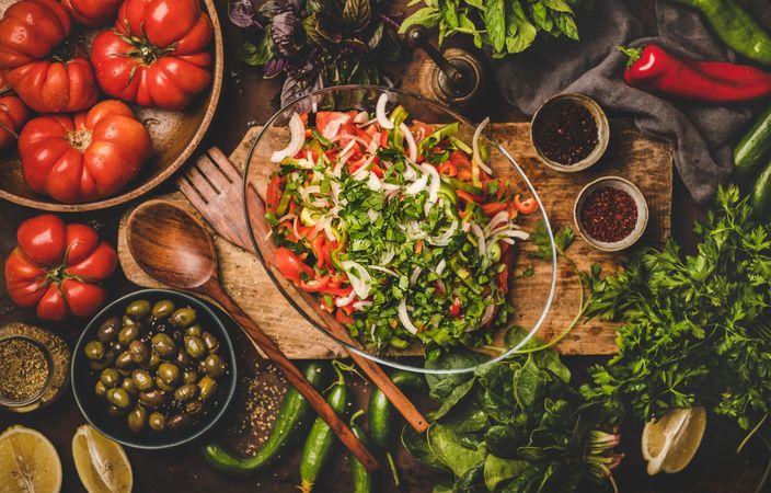 Fresh Mediterranean salad on wooden board surrounded with fresh vegetables and garnishes