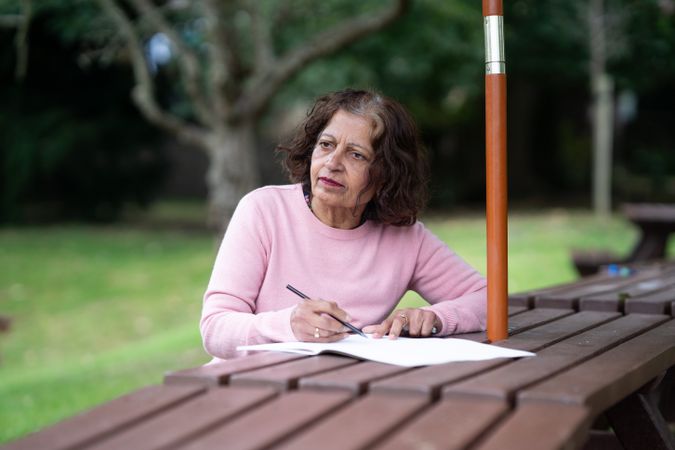 Older woman drawing in book on park bench