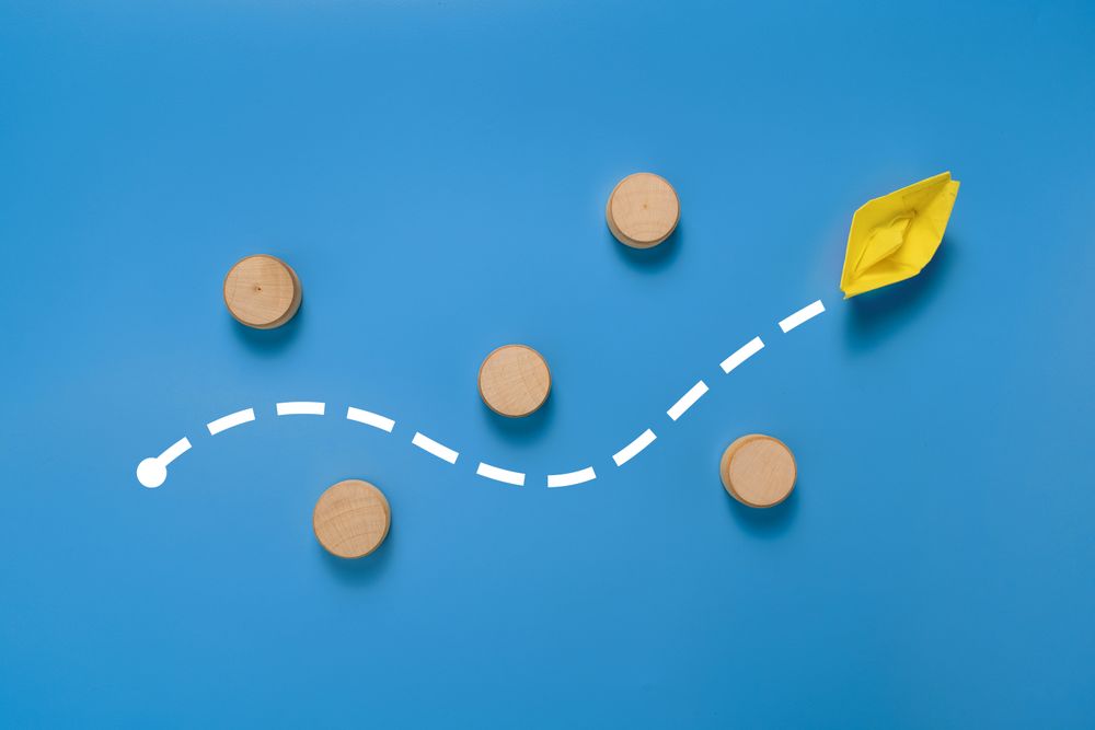 a yellow paper boat passes through barrier. isolated on blue background. concept of avoiding obstacle to achieve a goal