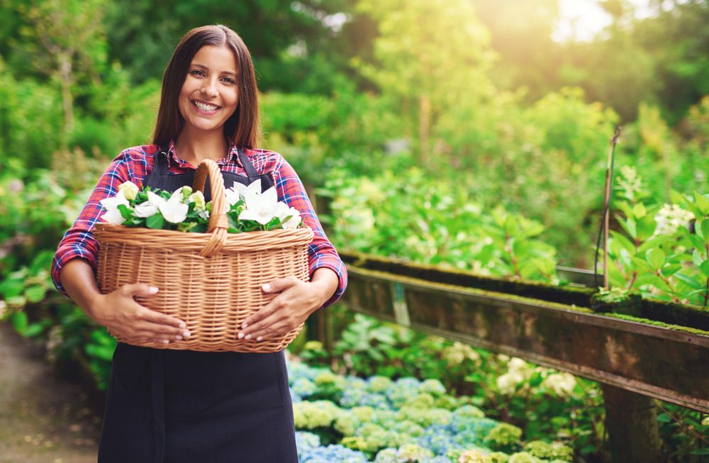 Smiling woman pictured in a greenhouse holding a basket of flowers