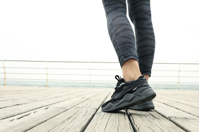 Female legs in leggings and sneakers on wooden floor outdoors, close up