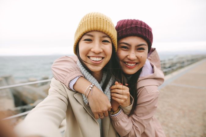 Selfie of two happy young Asian women hugging