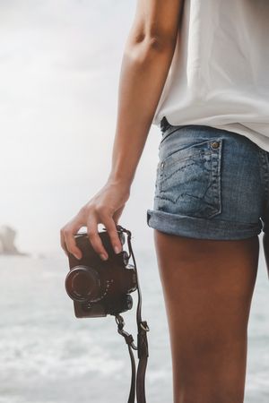 Woman with camera on shore near stones and water