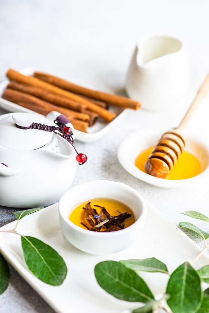 Cup of fragrant tea from pot served with honey dipper