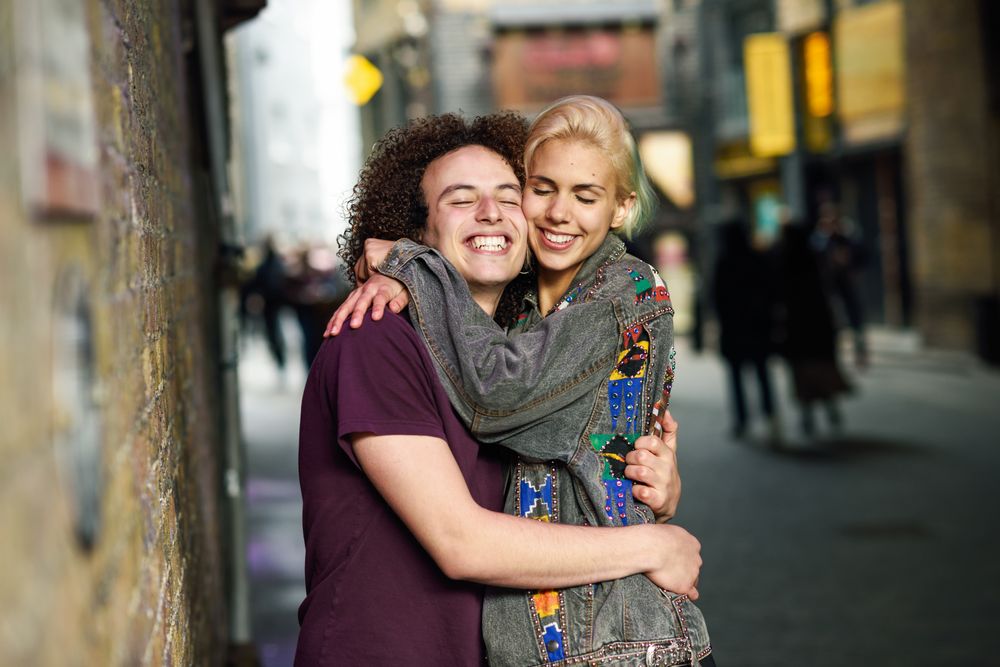 Male and female smiling and hugging with eyes closed on British city street