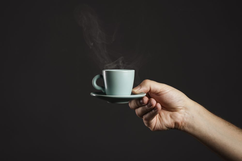 Hand holding a steaming cup of espresso coffee on a dark background.