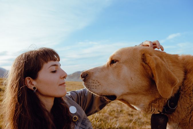 Woman with piercing sitting near dog between field