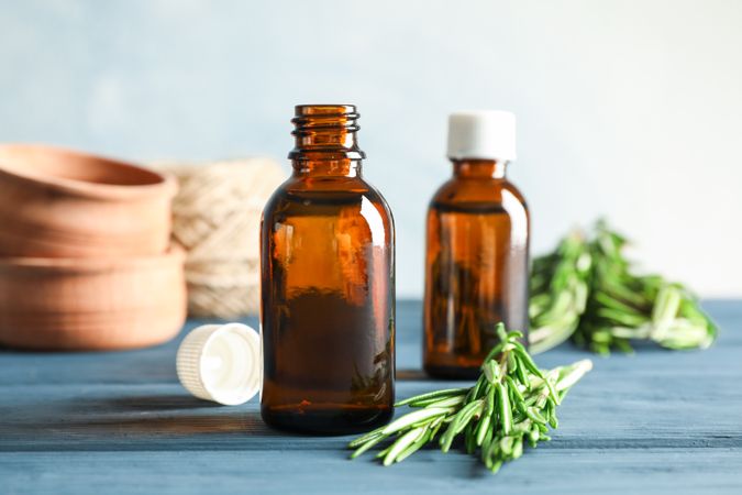 Rosemary oil and leaves, wood bowls on wooden background, space for text