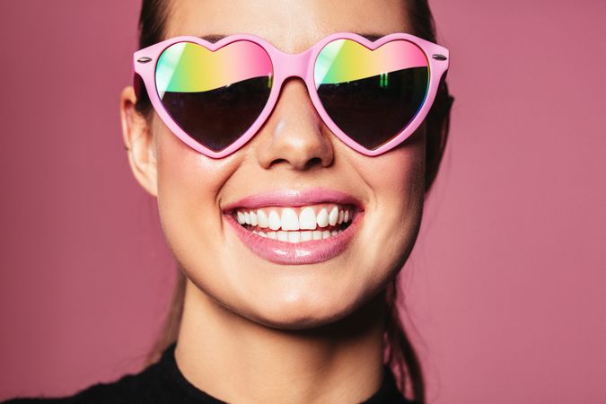 Smiling fresh faced woman in heart shape pink sunglasses