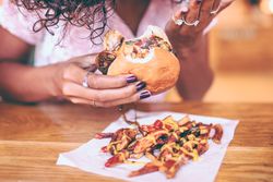 Young woman holding a bitten hamburger above loaded French fries