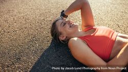 Woman athlete lying on ground relaxing during workout bGRKvA