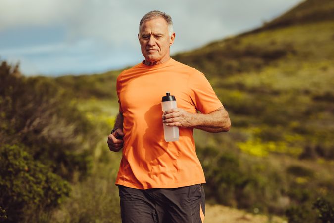 Fitness man jogging outdoors holding a water bottle