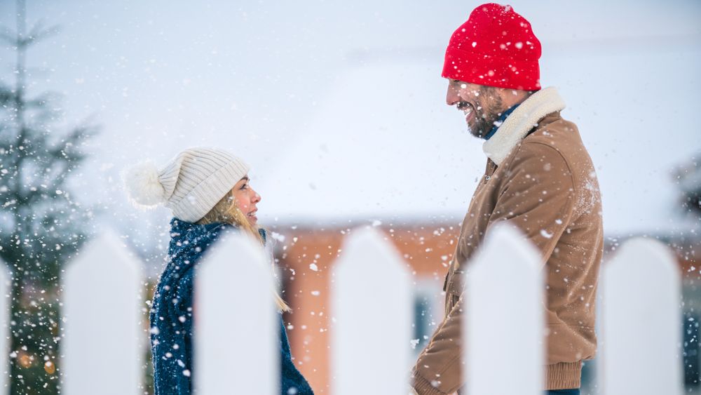 Young Couple Look into Each Other's Eyes and Happily Smile, Snow Falls on them. Couple in Love on the Backyard of Their Idyllic Home
