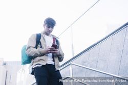 Man walking down stairs with backpack while using mobile outdoors 0WOOAP