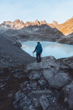 Back view of man with backpack standing on rock near lake in Switzerland