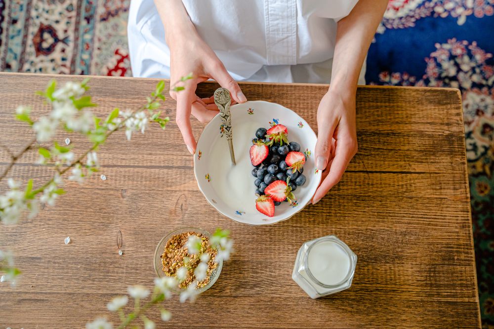 Top view of person preparing granola with yogurt and berries