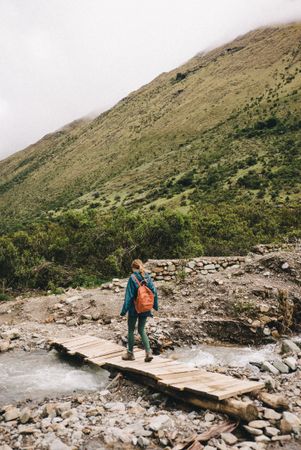 Female hiker walking on footbridge over river in Peruvian mountains