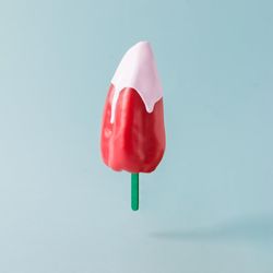 Red pepper with ice cream stick topped with pink syrup on pastel blue background