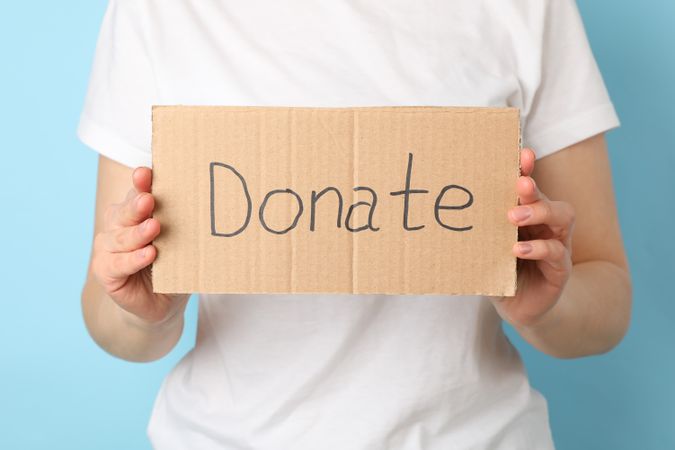 Woman holding cardboard with inscription Donate on blue background