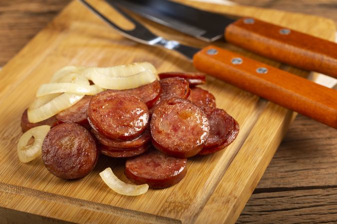 Sliced calabrese sausage with onion on wooden background.