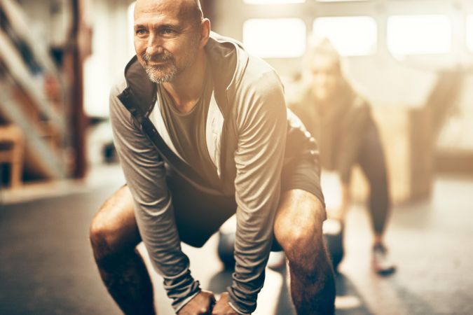 Man squatting in grey hoodie in gym