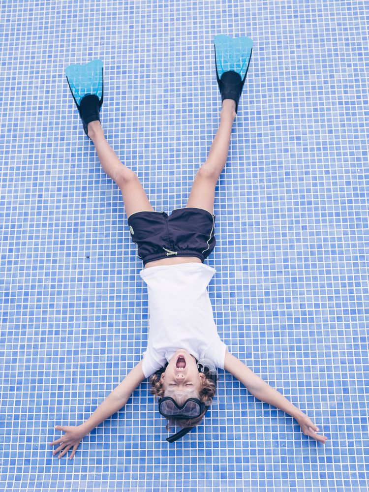 Adorable boy in snorkeling mask and flippers lying on pool