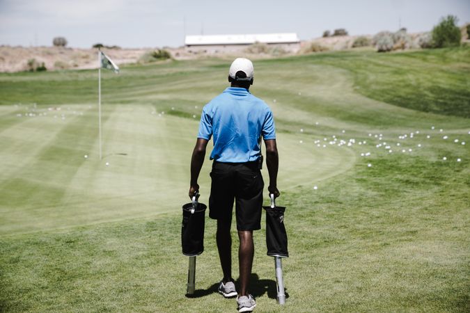 Back view of Black man with golf club walking on green grass field