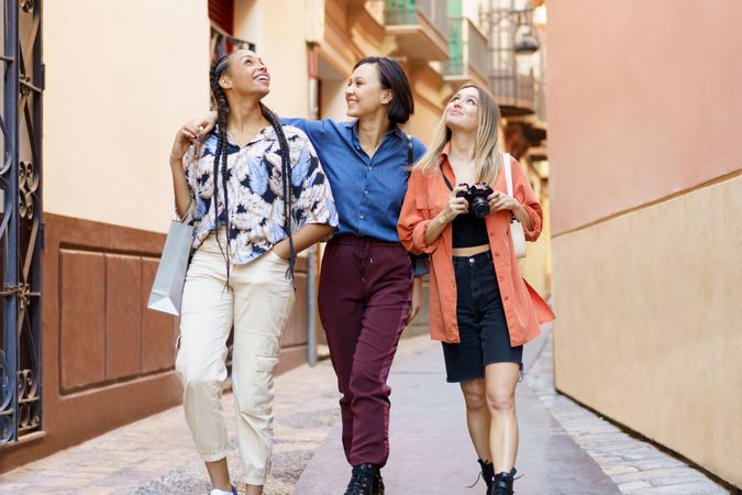 Three women strolling down narrow lane with camera and looking around