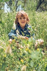 Cheerful adorable boy sitting with crossed legs in green meadow