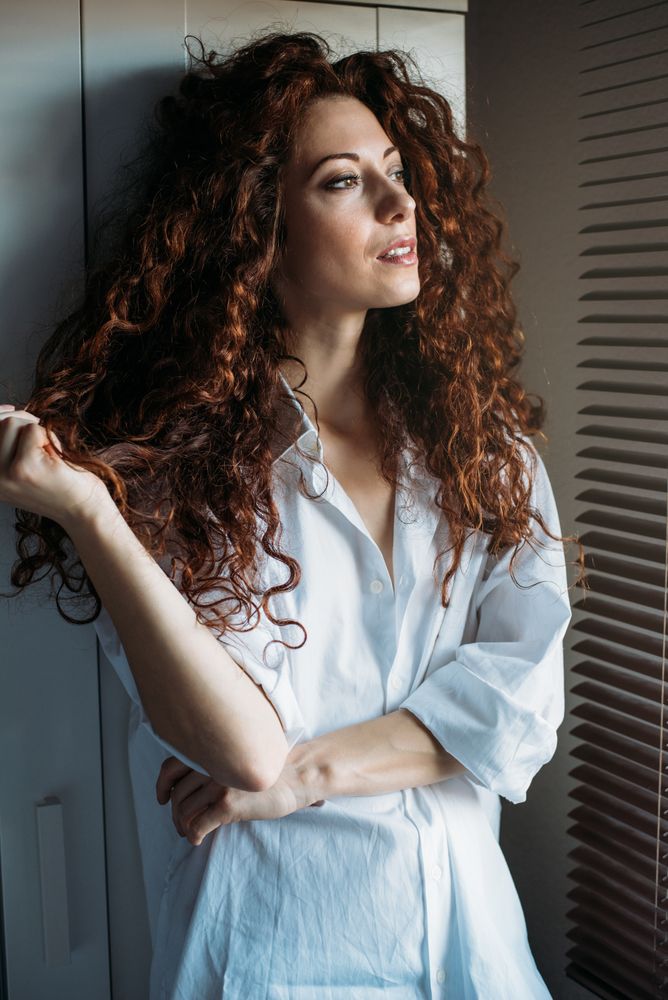 Beautiful thoughtful woman standing by a windows blind
