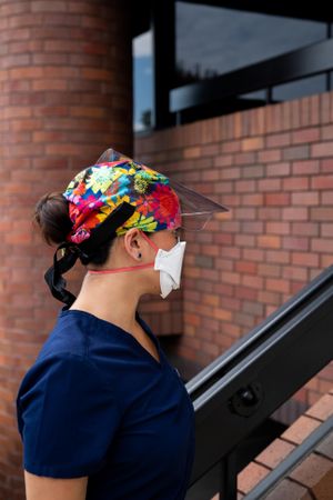 Profile of woman nurse with flowered hair covering, N95 and face shield standing outside