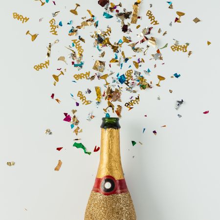 Golden champagne party bottle on light  background with multi-colored confetti