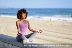 Black woman with afro hairstyle meditating on the beach 4NzaD4