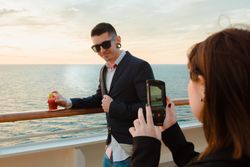 Woman taking photo of man on deck of ship at sea