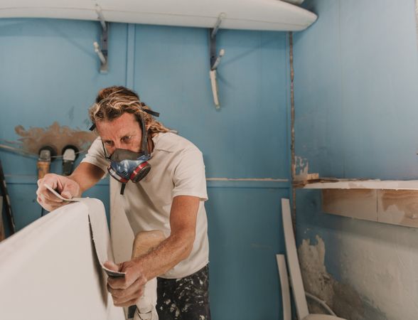 Man in respirator measuring surf board in workshop