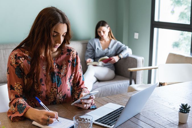 Focused woman taking notes and working on laptop