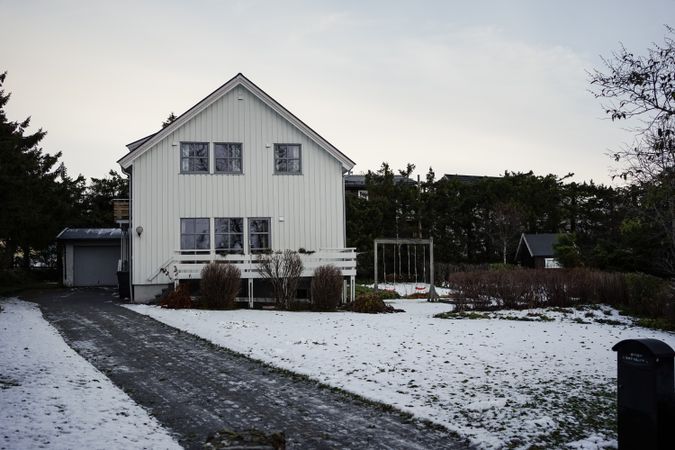 Large red barn against snowy hill and residential houses in countryside
