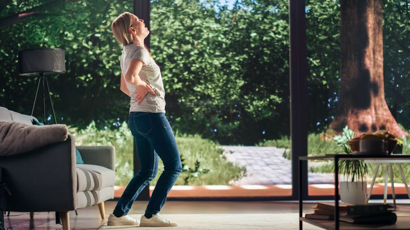 Young Adult Female Standing Up from a Couch at Home and Experiencing Back Pain in a Result of Spine Trauma.