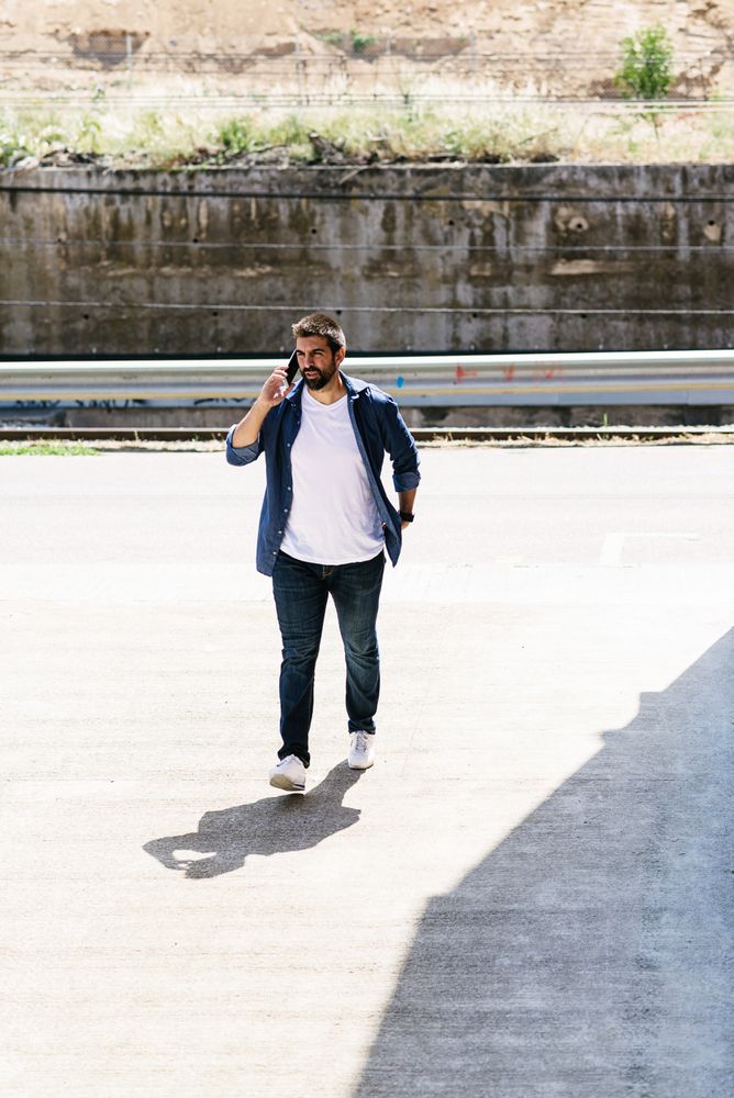 Man in denim walking outside by river talking on phone