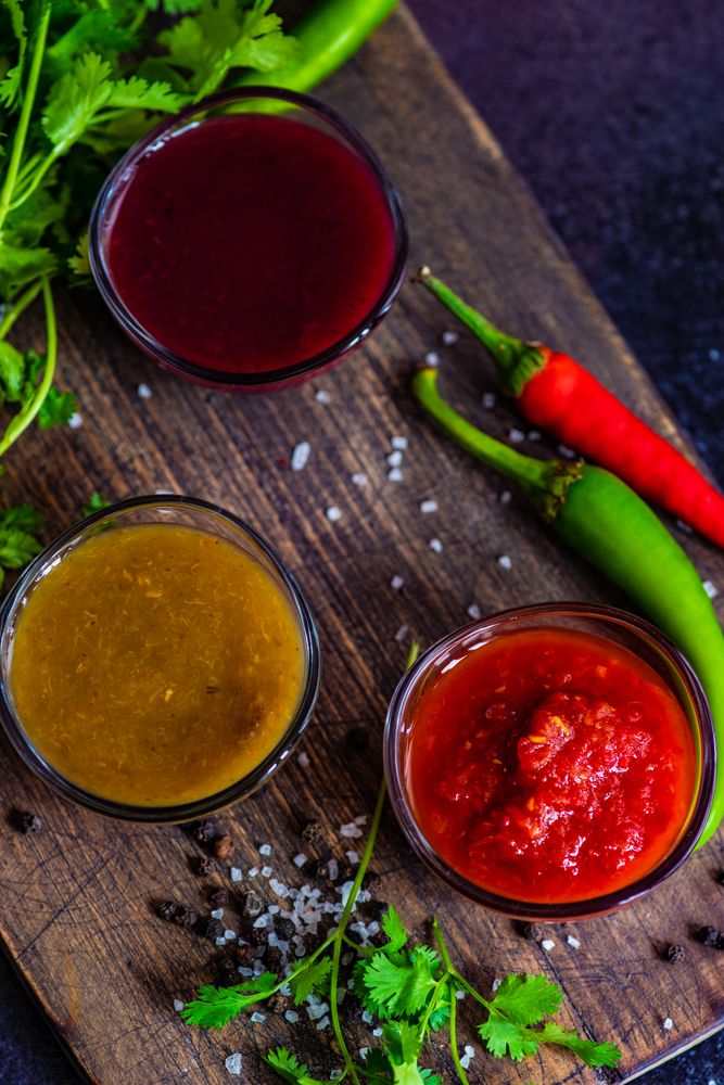 Close up of three traditional Georgian condiments tomato satsebeli, yellow and red tkemali with ingredients on cutting board