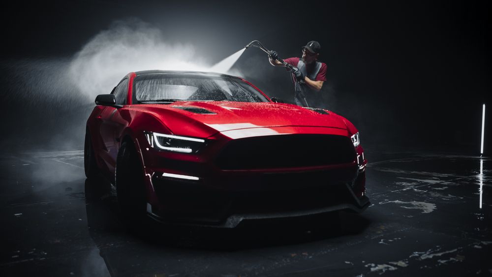 Adult Car Washer in Uniform Washing a Red Performance Car with a High Pressure Cleaner.