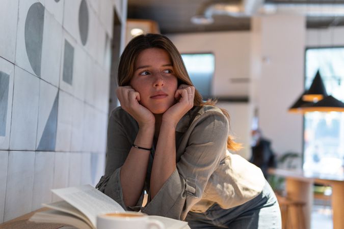 Dreamy woman with book and coffee in cafe