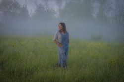 Woman shepherd standing n a grass field in the fog 56V9l5