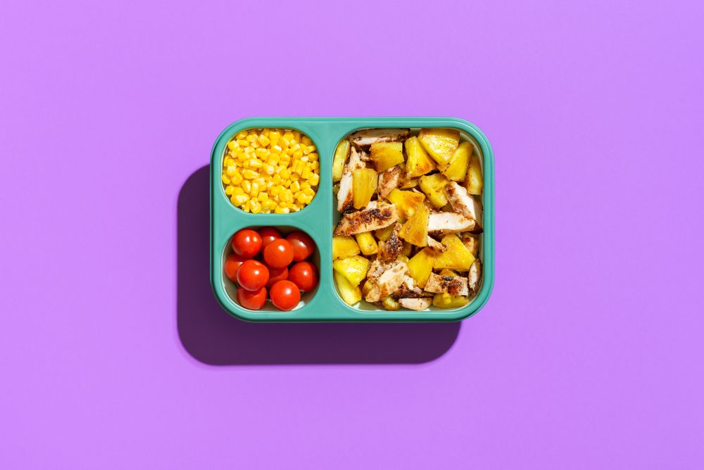 Summer salad in a lunch box, top view on purple background