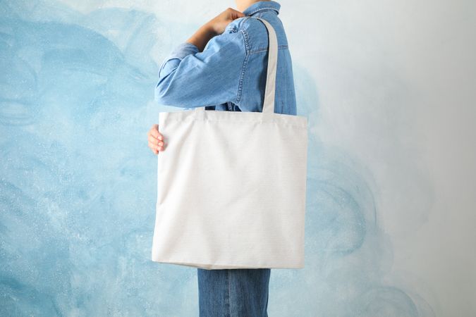 Young woman holding tote bag against blue background, empty space